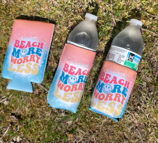 Three bottles with colorful 'Beach More Worry Less' labels on a grassy surface.