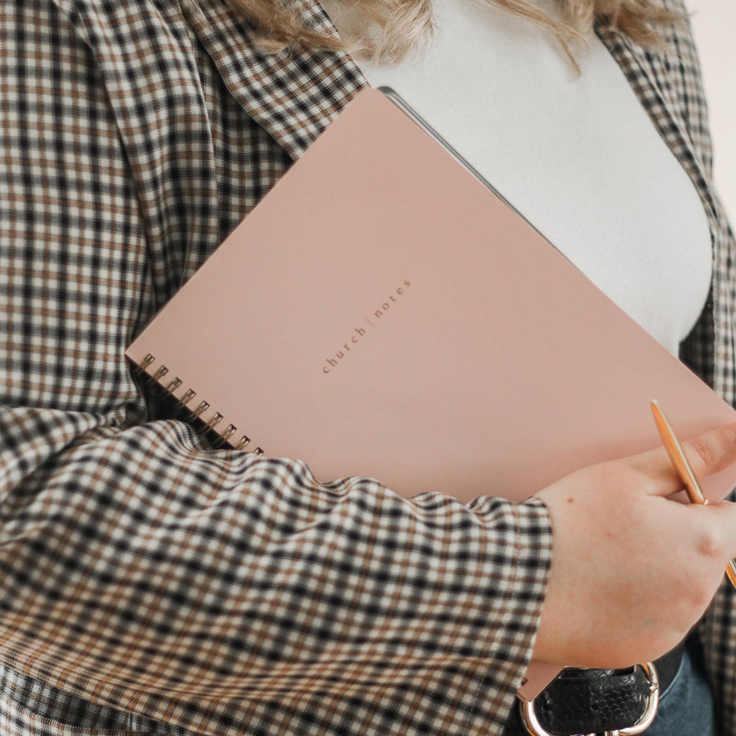 Person holding a pink notebook with 'church notes' written on it, wearing a plaid shirt.