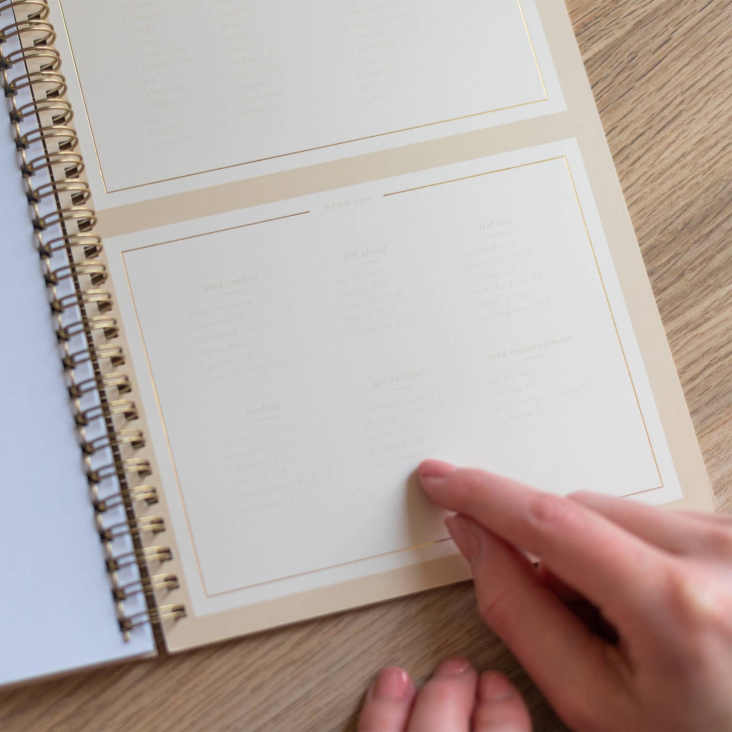 Hand holding a spiral-bound notebook with blank pages on a wooden surface