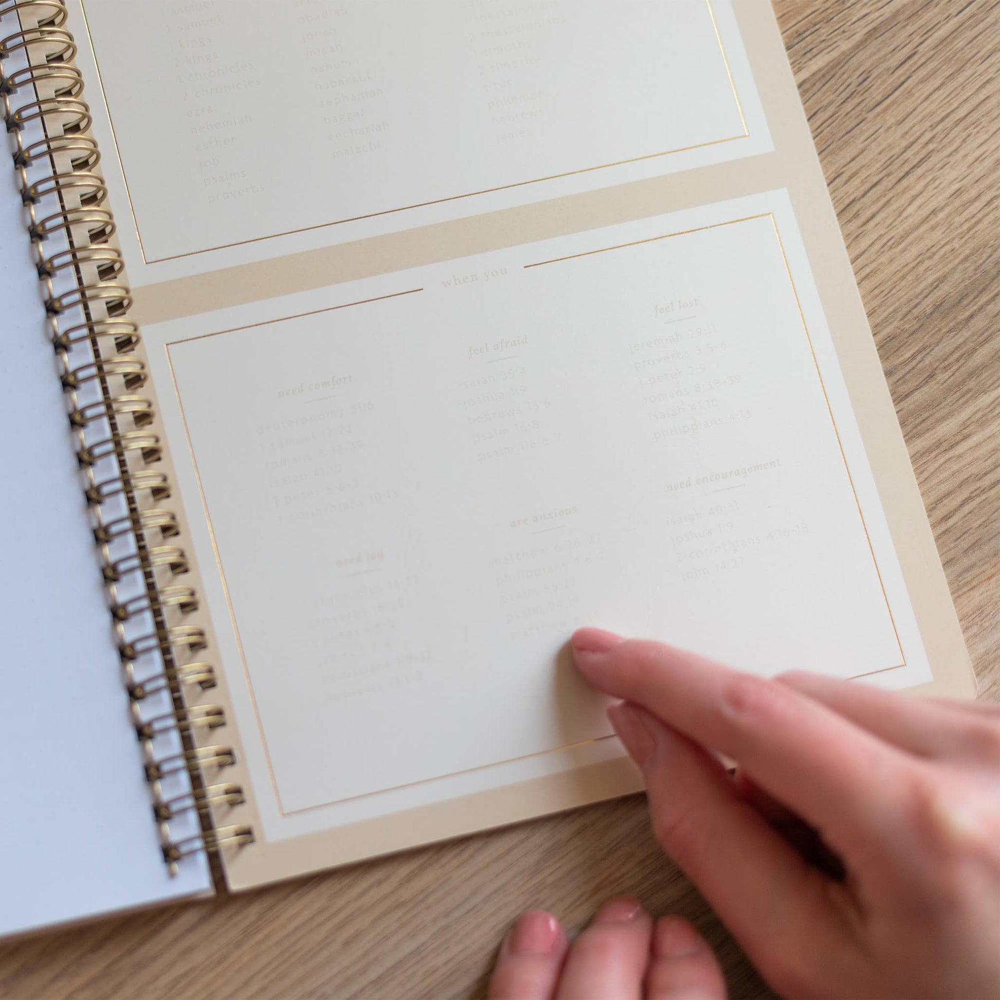 Hand holding a spiral-bound notebook with blank pages on a wooden surface