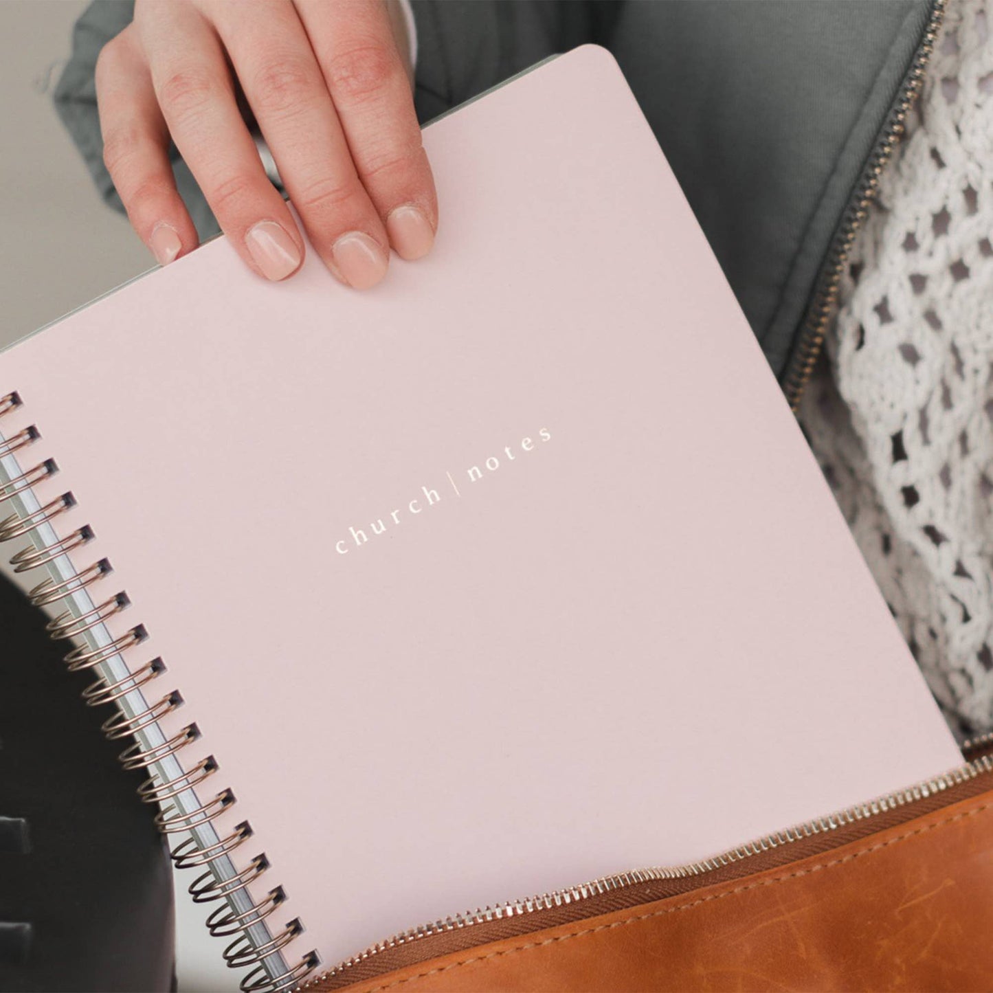 Pink notebook with 'church notes' text held by a hand, placed on a textured surface.