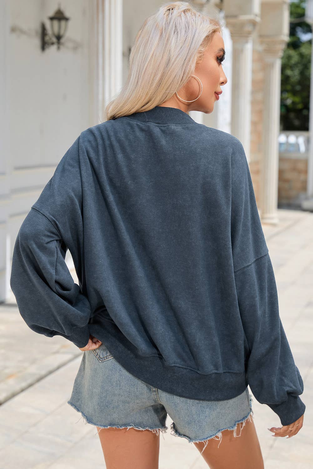 Woman wearing a dark blue oversized sweatshirt and denim shorts outdoors.