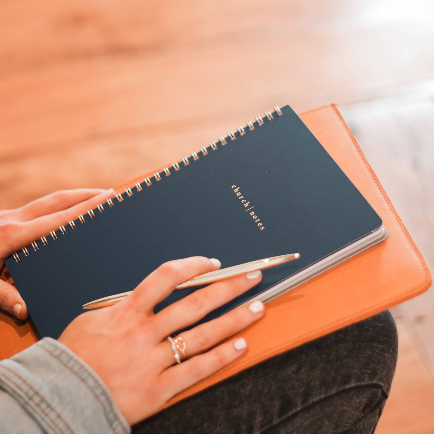 Person holding a black notebook with a pen on an orange surface