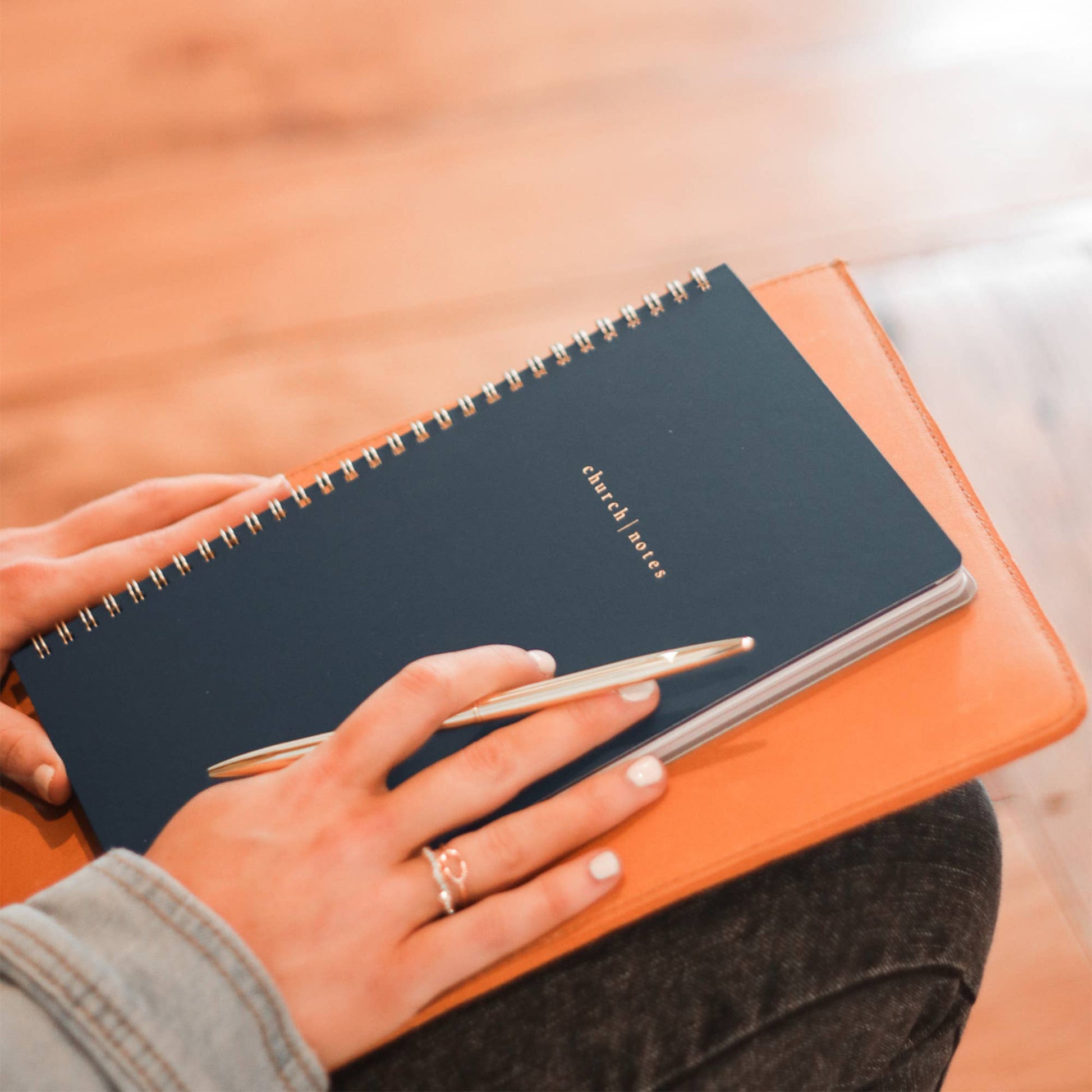 Person holding a black notebook with a pen on an orange surface
