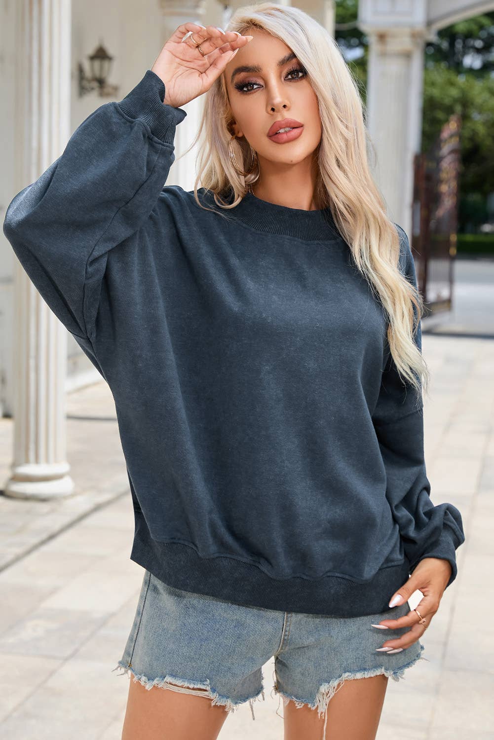 Woman wearing a dark blue sweatshirt and denim shorts outdoors.