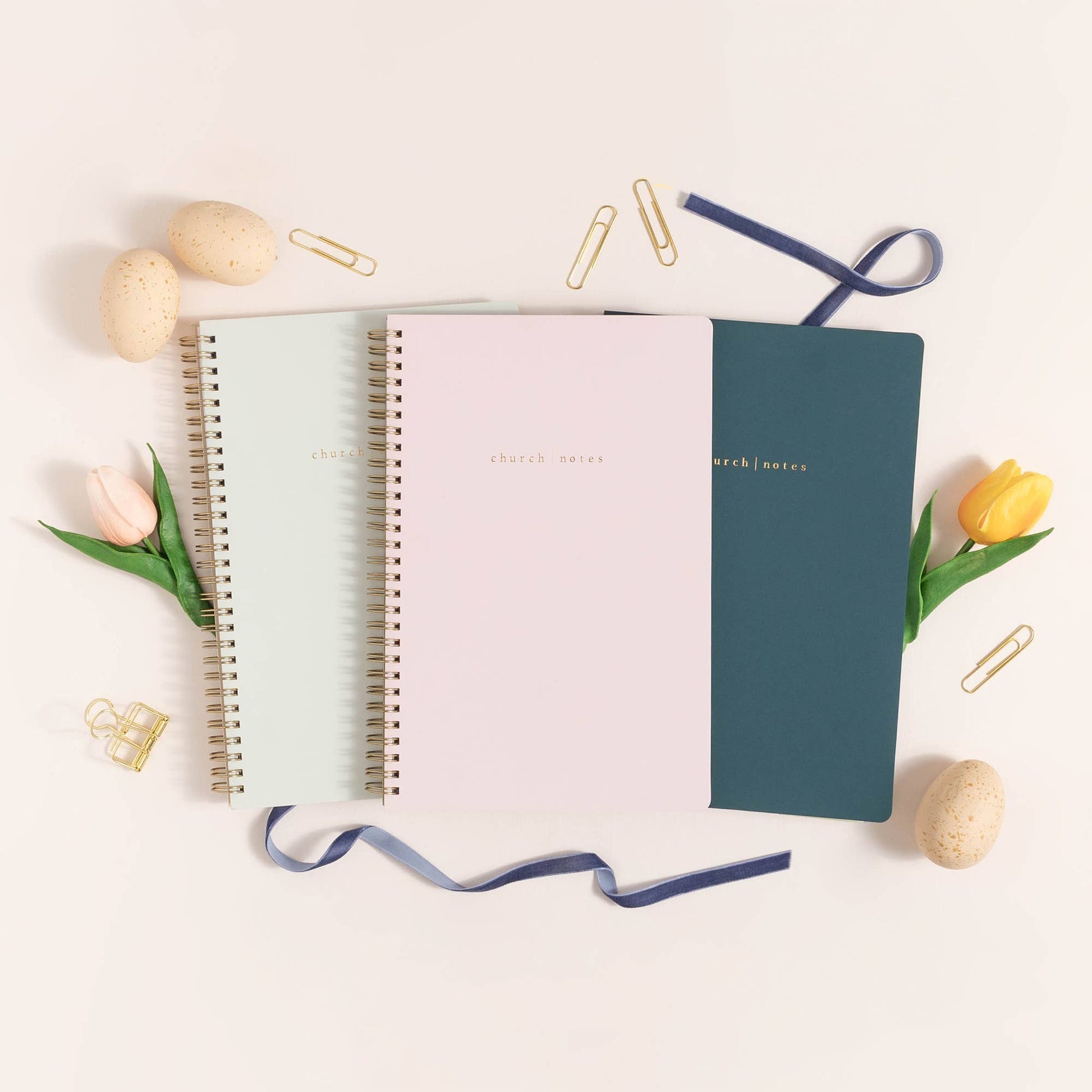 Three spiral-bound notebooks in pastel colors with decorative elements on a light background