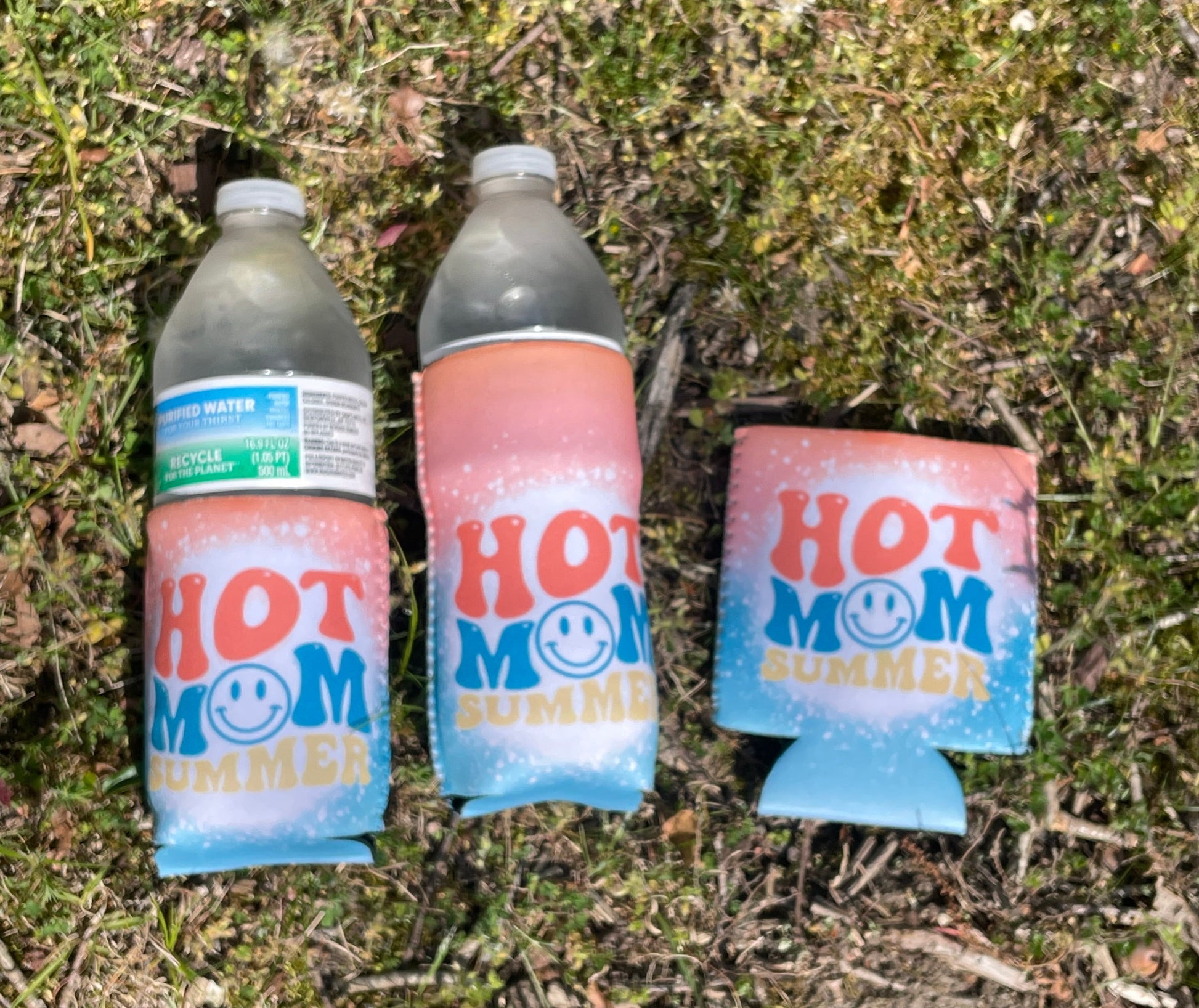 Three bottles with 'Hot Mom' branding on a grassy surface