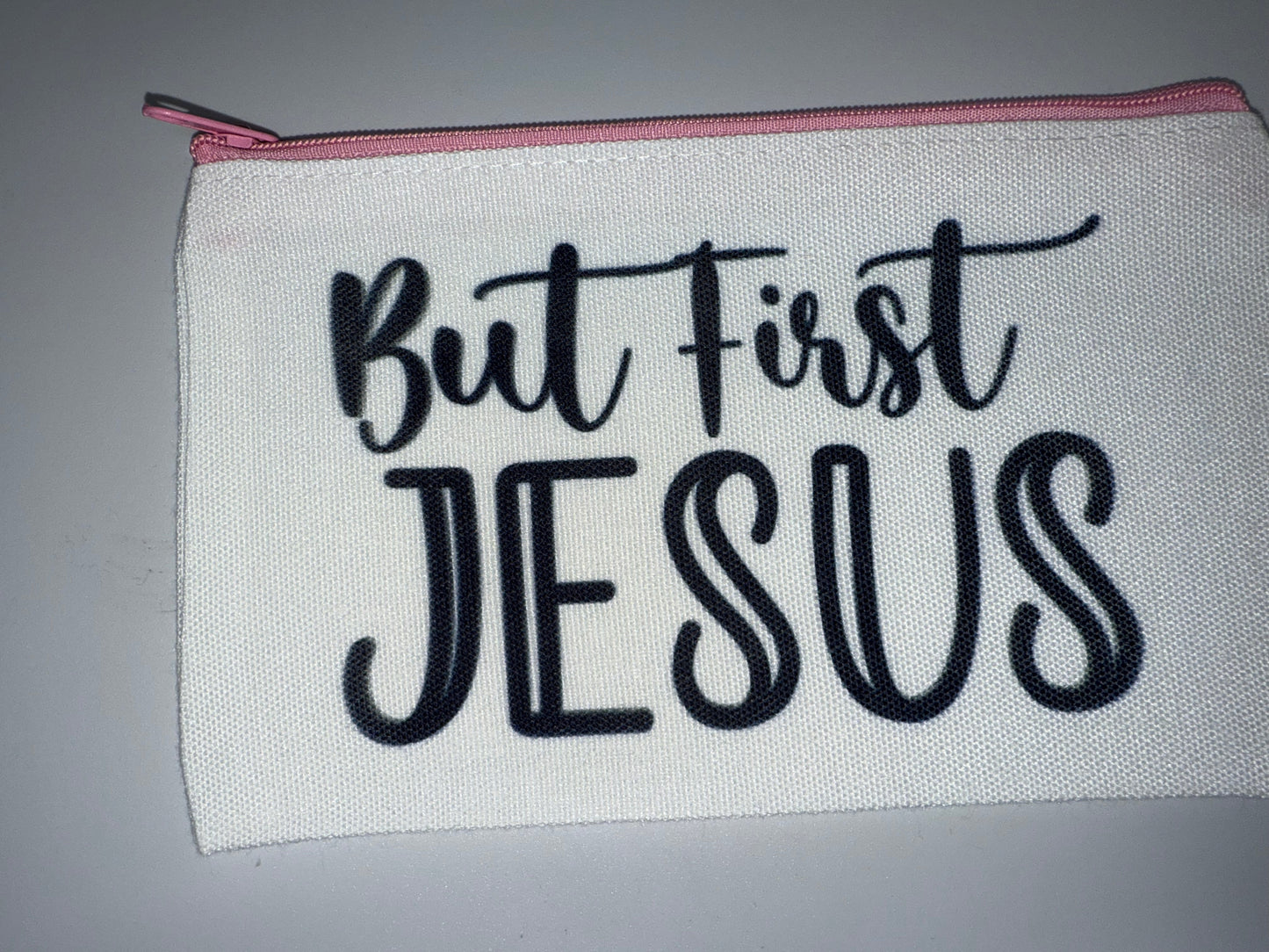 White pouch with 'But first, Jesus' text on a gray background