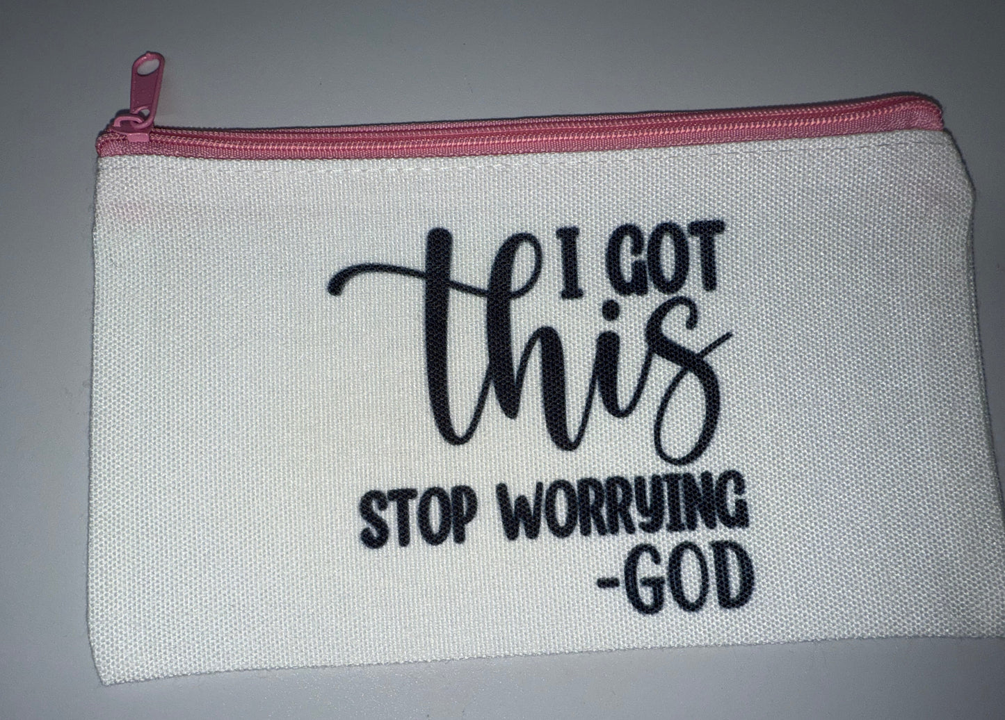 White pouch with motivational text 'I got this stop worrying God' on a gray background