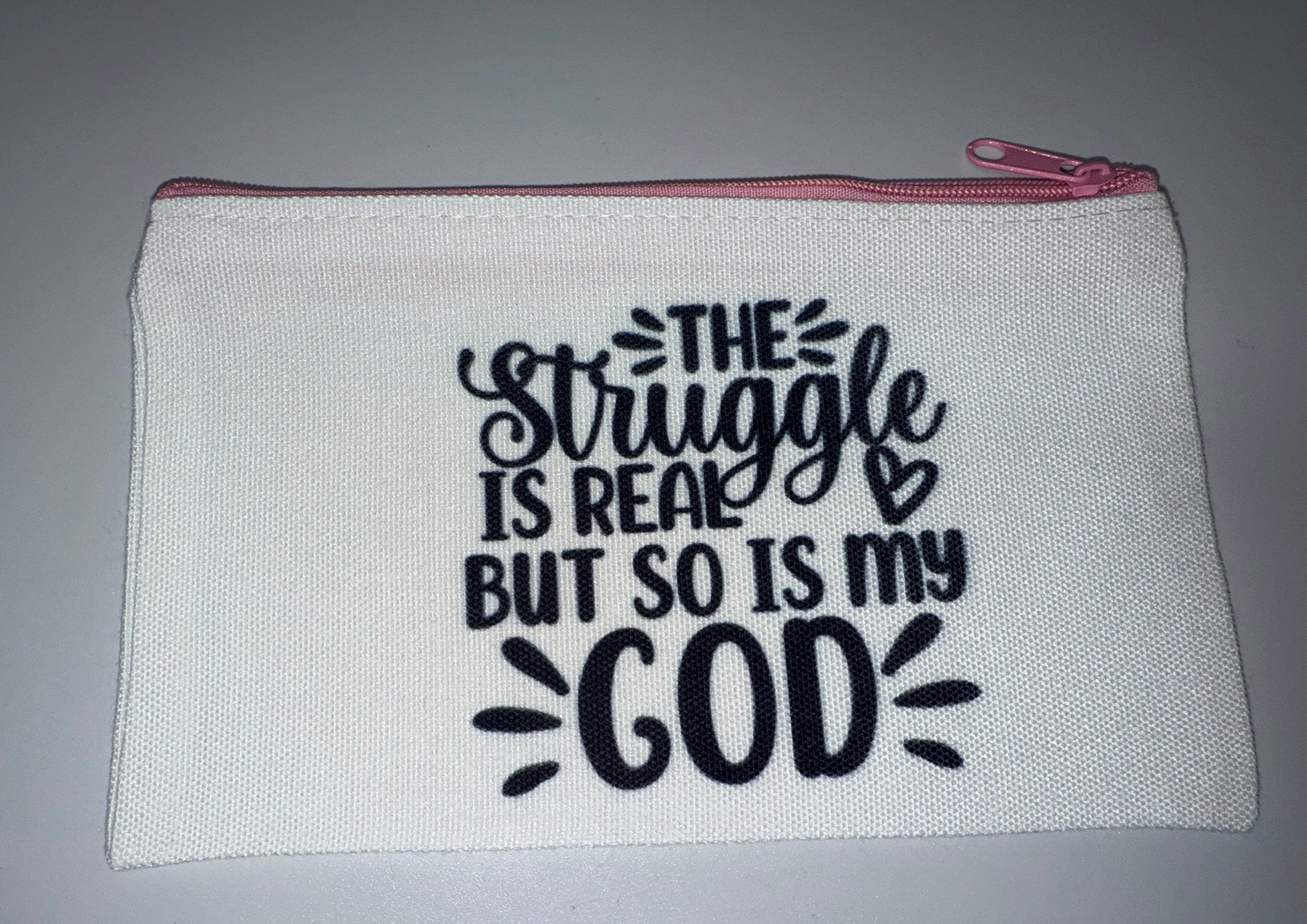 White pouch with black text 'The struggle is real, but so is God' on a gray background