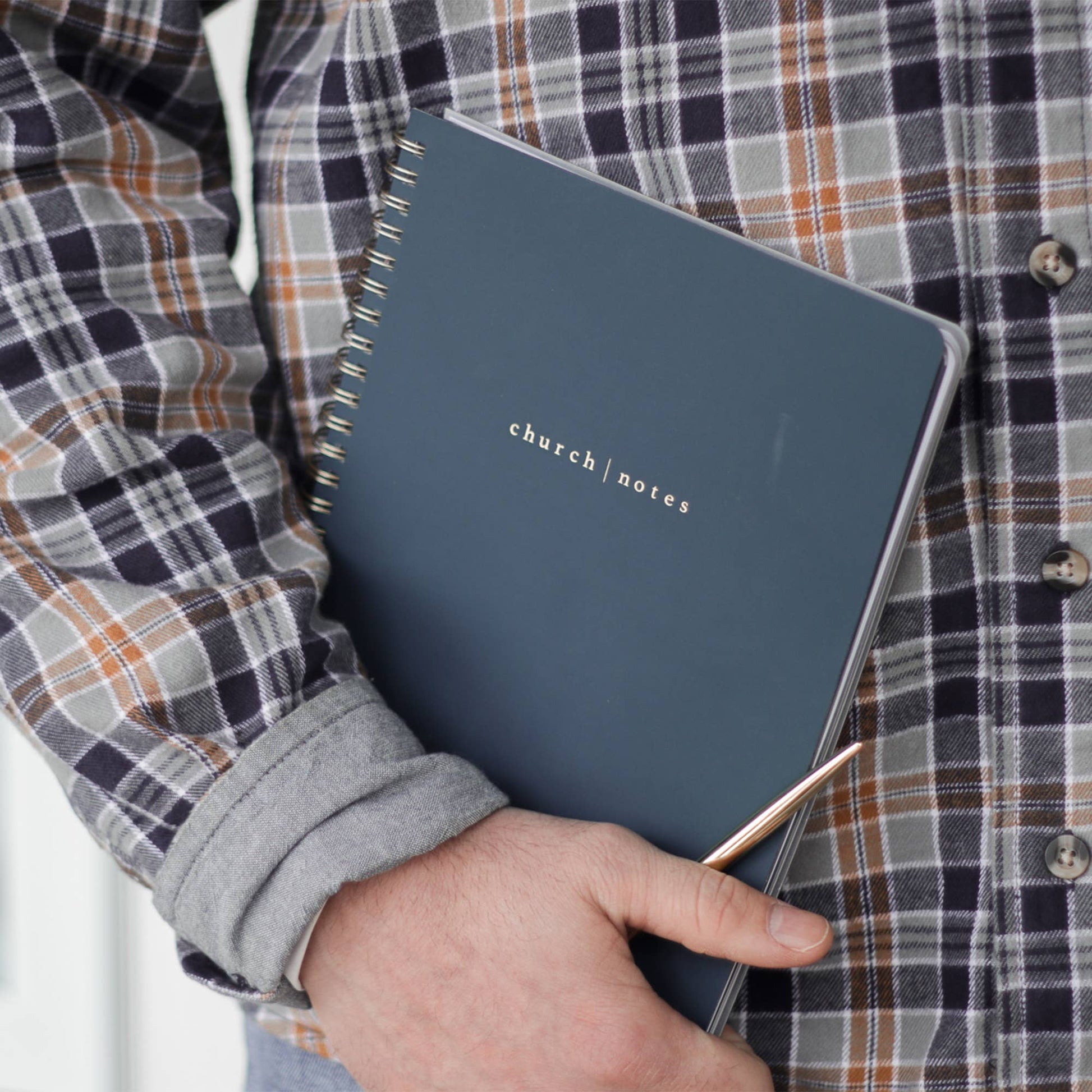 Person holding a blue notebook labeled 'church notes' against a plaid shirt background