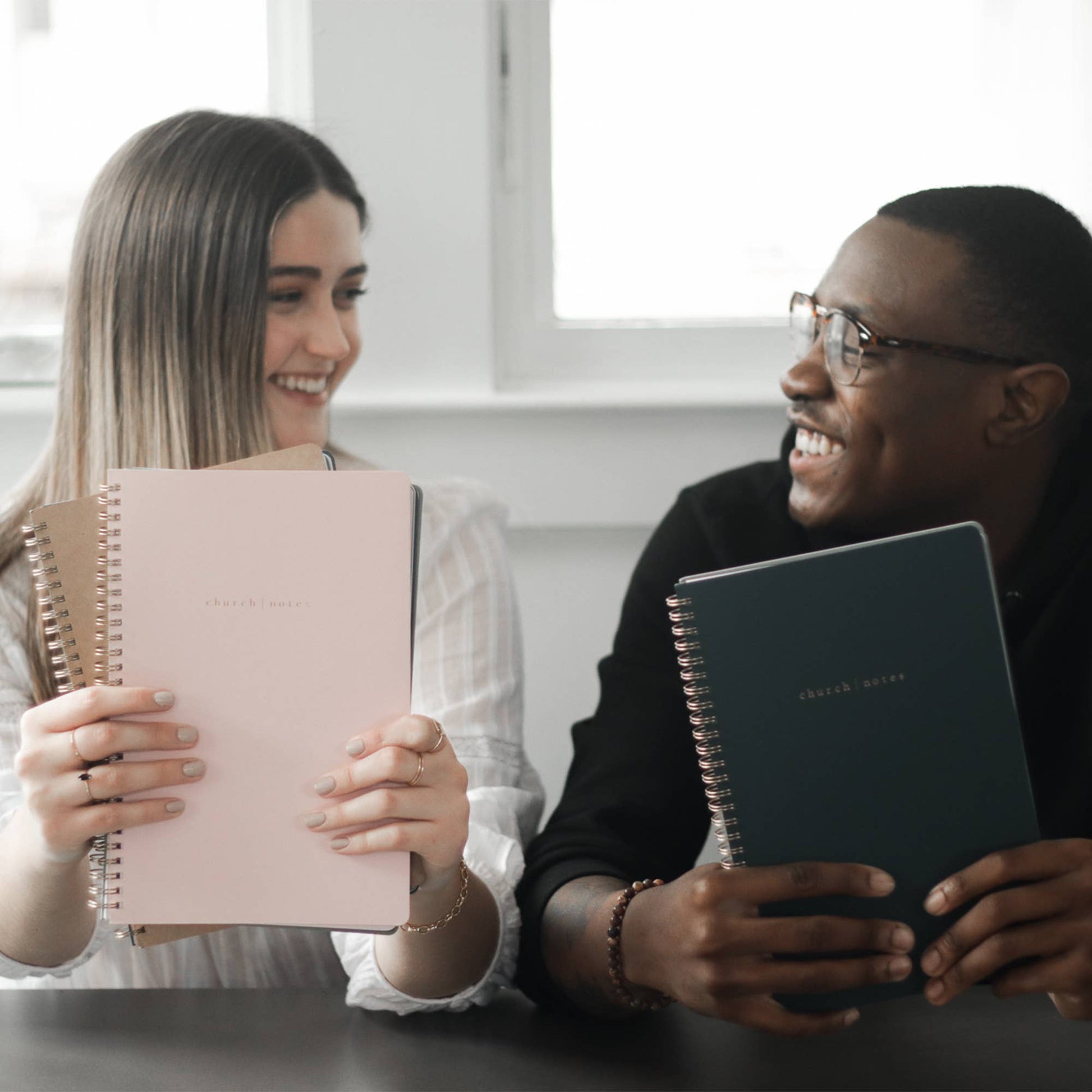 Two people holding notebooks and smiling at each other.