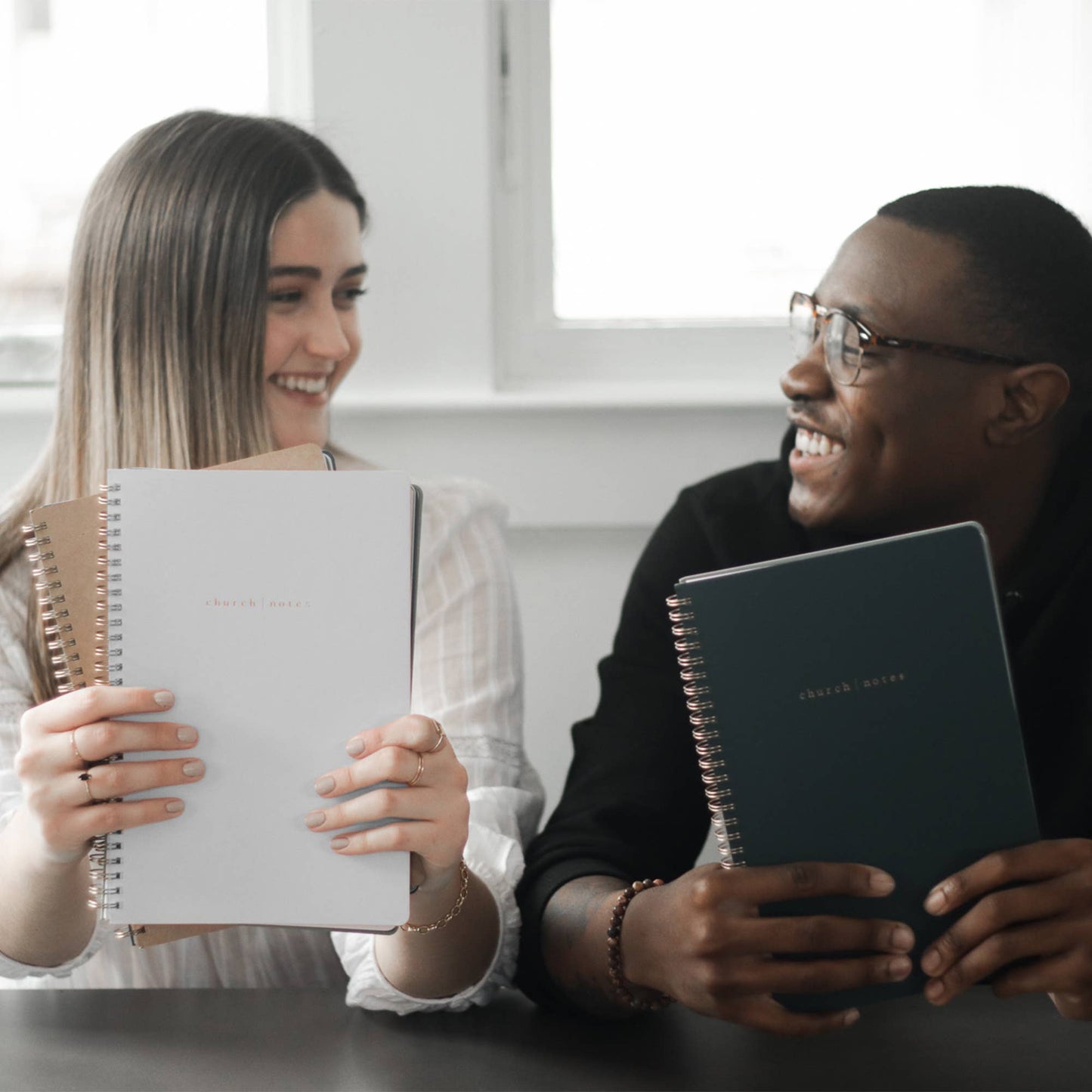 Two people holding notebooks and smiling at each other.