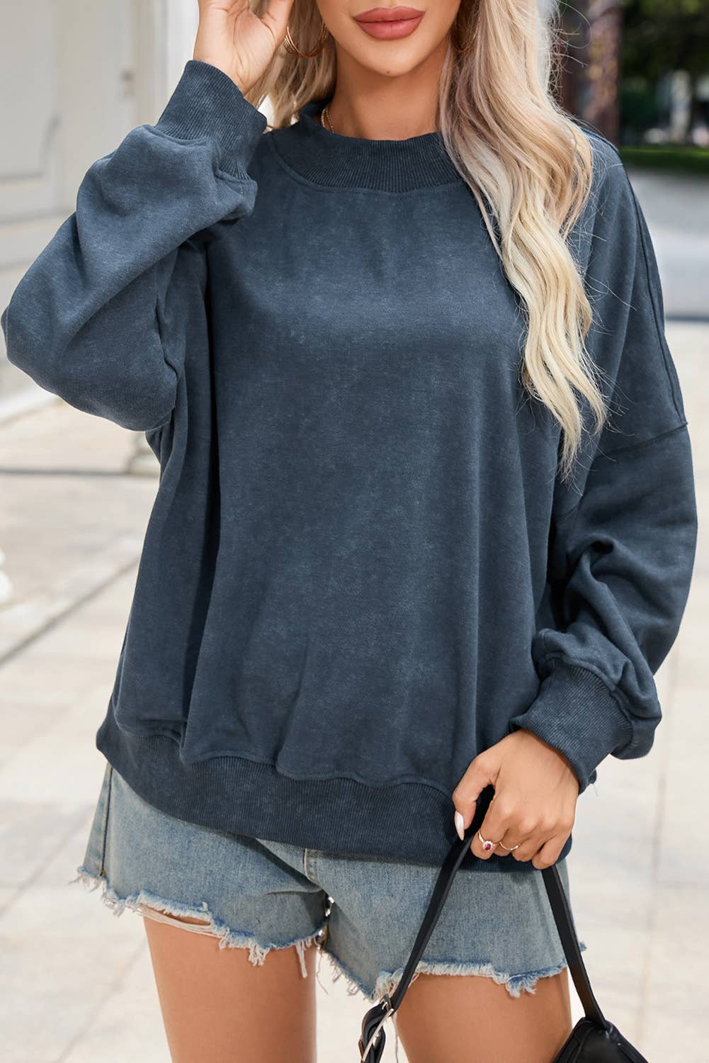 Person wearing a blue sweatshirt and denim shorts outdoors.